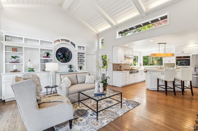 living room with light wood-style floors, beam ceiling, a healthy amount of sunlight, and high vaulted ceiling
