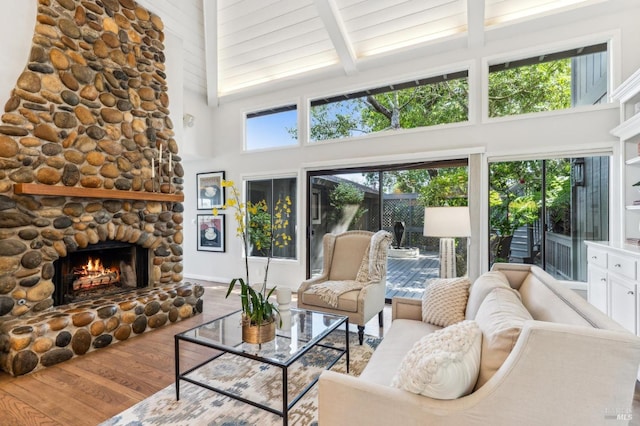 living room featuring beamed ceiling, high vaulted ceiling, a stone fireplace, and wood finished floors