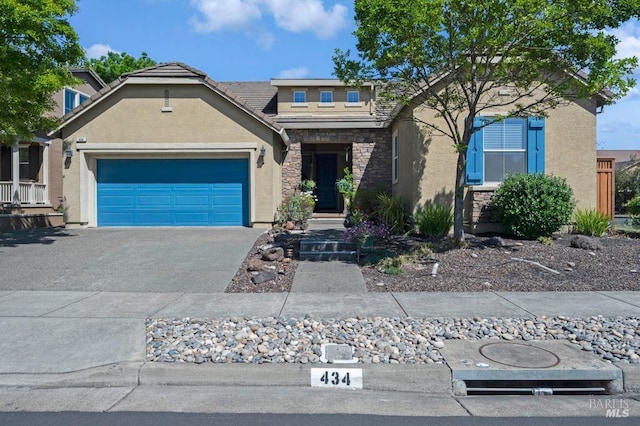 view of front of property featuring a tile roof, stone siding, a garage, stucco siding, and driveway