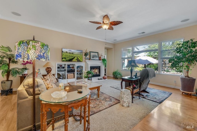 living area featuring crown molding, a ceiling fan, baseboards, wood finished floors, and visible vents