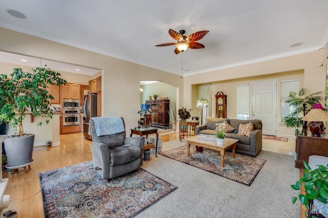 living room with crown molding, arched walkways, ceiling fan, and light wood finished floors