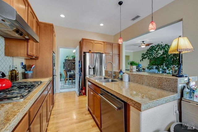 kitchen with appliances with stainless steel finishes, a sink, light wood-style flooring, under cabinet range hood, and pendant lighting