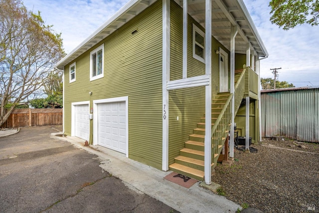 view of home's exterior with stairway, aphalt driveway, fence, and a garage