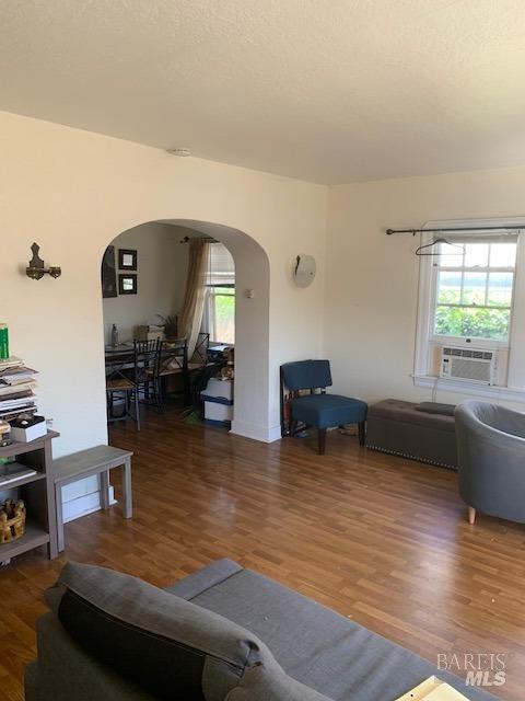 living room featuring a healthy amount of sunlight, arched walkways, cooling unit, and wood finished floors