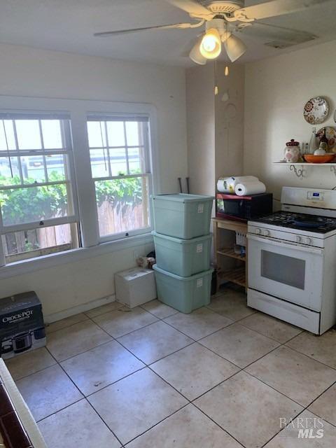 kitchen featuring white gas range, ceiling fan, stainless steel microwave, and light tile patterned flooring