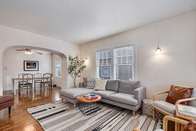 living area featuring baseboards, arched walkways, a ceiling fan, and wood finished floors