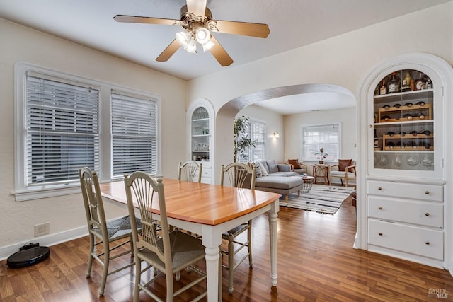 dining room featuring baseboards, arched walkways, ceiling fan, and wood finished floors