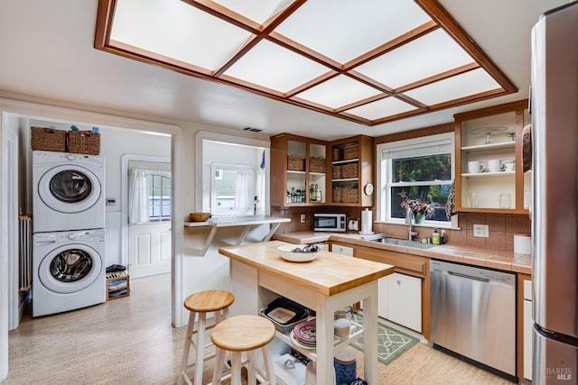 kitchen featuring open shelves, stacked washing maching and dryer, tile counters, a sink, and stainless steel appliances