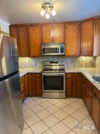 kitchen with brown cabinets, backsplash, appliances with stainless steel finishes, and light tile patterned floors