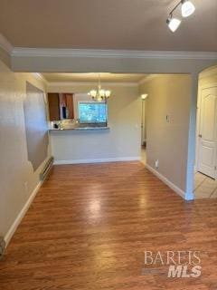 unfurnished dining area with crown molding, baseboards, wood finished floors, and a notable chandelier