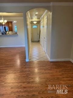 hall with crown molding, an inviting chandelier, arched walkways, baseboards, and wood finished floors
