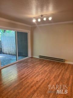empty room featuring crown molding, baseboards, wood finished floors, and a baseboard radiator