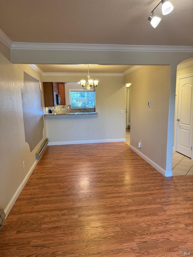 empty room with crown molding, baseboard heating, light wood-style flooring, and a notable chandelier