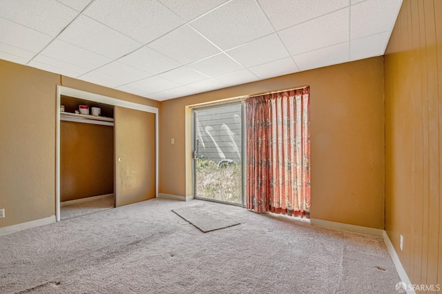 unfurnished bedroom with baseboards, carpet, a drop ceiling, and a closet