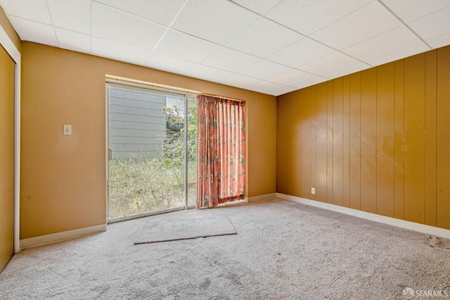 carpeted spare room with baseboards, a drop ceiling, and wooden walls