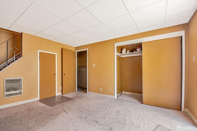unfurnished bedroom with carpet floors, heating unit, a paneled ceiling, and a closet