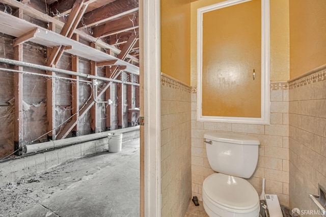 bathroom featuring a wainscoted wall, toilet, and tile walls