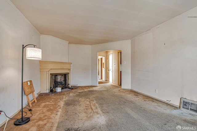 unfurnished living room featuring visible vents, crown molding, carpet flooring, a fireplace with raised hearth, and arched walkways