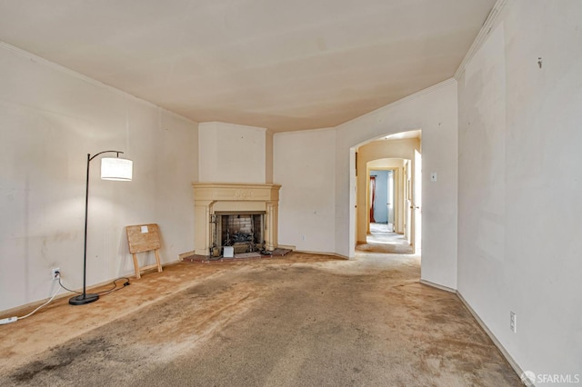unfurnished living room featuring carpet flooring, crown molding, arched walkways, a fireplace with raised hearth, and baseboards