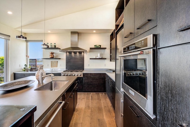 kitchen with wall chimney range hood, dark brown cabinets, open shelves, a sink, and light wood-type flooring