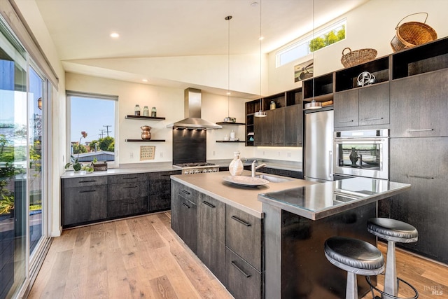 kitchen with open shelves, wall chimney range hood, a sink, light wood-style flooring, and appliances with stainless steel finishes