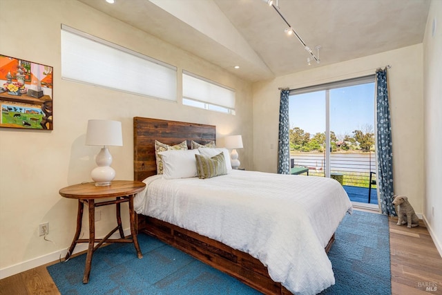 bedroom with wood finished floors, baseboards, access to outside, rail lighting, and vaulted ceiling