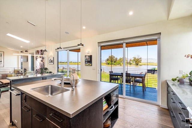 kitchen with dark brown cabinets, a sink, light wood-style floors, an island with sink, and pendant lighting