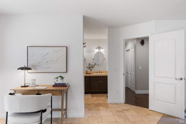 corridor with light tile patterned flooring, baseboards, and a sink