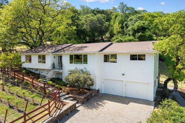 ranch-style house with roof with shingles, fence, an attached garage, and decorative driveway