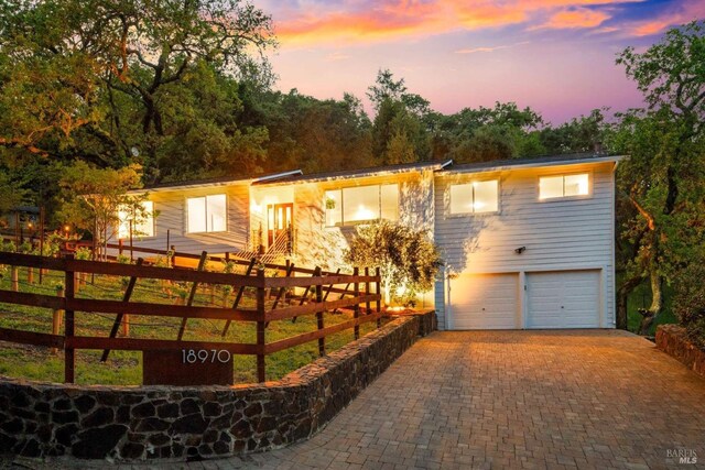 view of front of home with an attached garage, decorative driveway, and fence