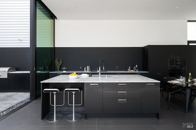 kitchen with a sink, light stone counters, modern cabinets, and dark tile patterned flooring