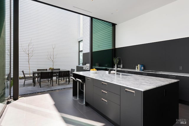 kitchen featuring a kitchen island with sink, light stone counters, modern cabinets, dark cabinets, and a sink