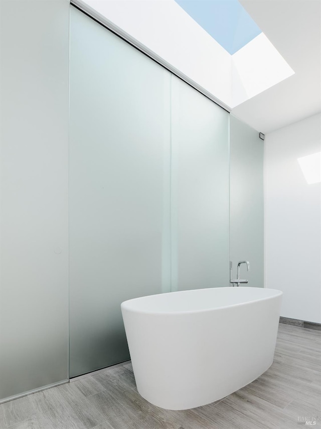bathroom featuring wood finished floors, a skylight, and a soaking tub