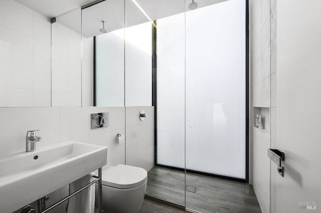 bathroom with wood finished floors, toilet, tile walls, walk in shower, and a sink