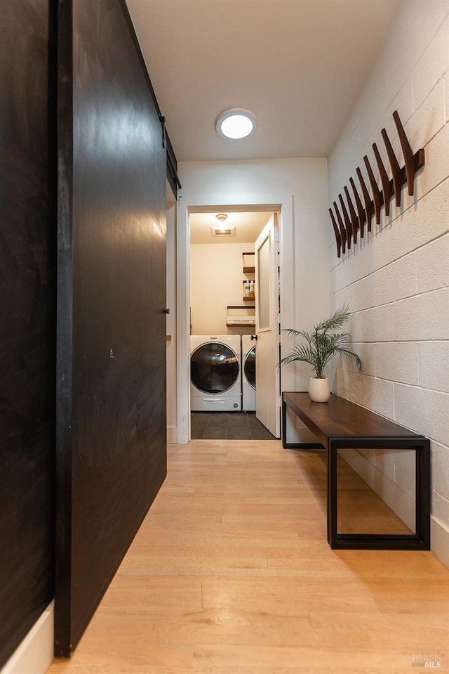 hall featuring independent washer and dryer, a barn door, and light wood finished floors