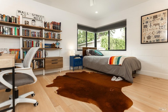 bedroom featuring concrete block wall, recessed lighting, and wood finished floors