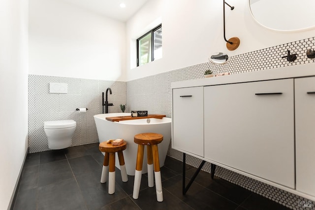 bathroom with wainscoting, tile patterned flooring, toilet, tile walls, and a soaking tub
