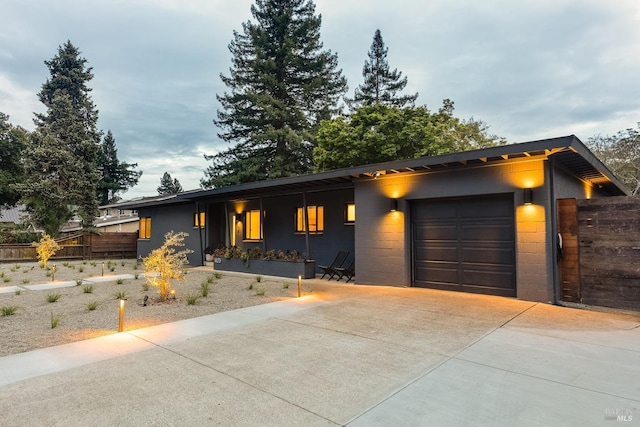 view of front of house with fence, an attached garage, driveway, and concrete block siding