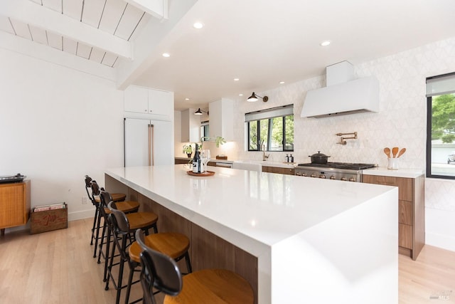 kitchen featuring light wood-style floors, range hood, built in fridge, white cabinets, and stainless steel gas stovetop