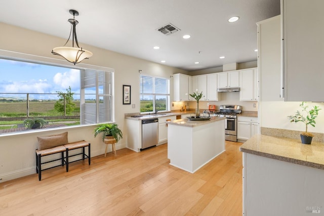 kitchen featuring visible vents, a kitchen island, under cabinet range hood, white cabinets, and stainless steel appliances