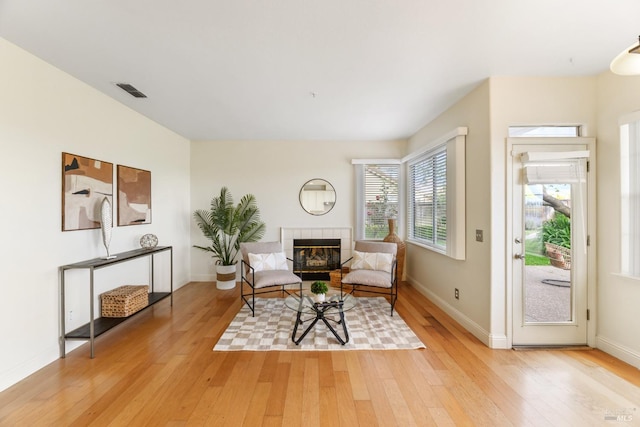 living area with baseboards, visible vents, a tile fireplace, and light wood-type flooring