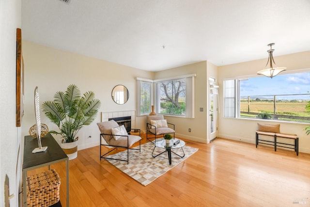 sitting room with a tiled fireplace, baseboards, and light wood-type flooring