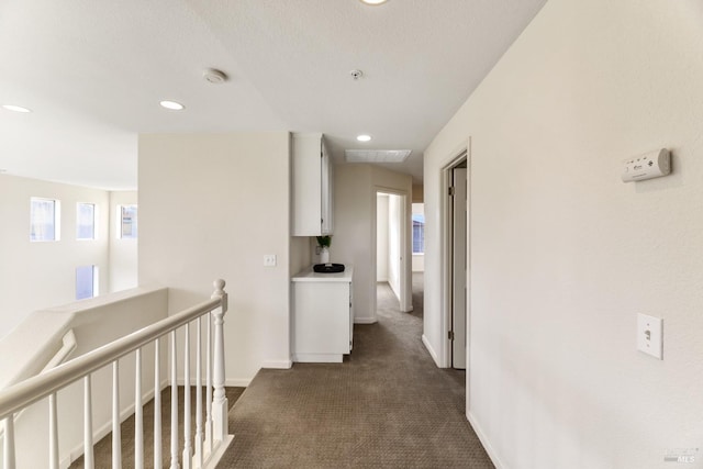 hall featuring dark carpet, recessed lighting, baseboards, and an upstairs landing