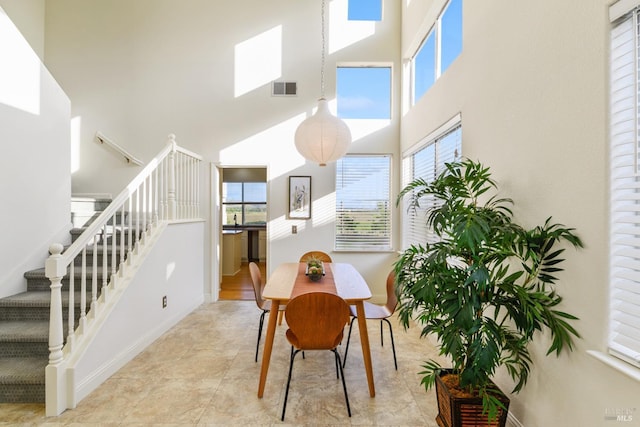 dining room with stairway, baseboards, visible vents, and a towering ceiling