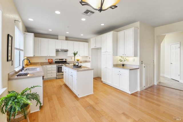 kitchen featuring under cabinet range hood, white cabinets, stainless steel range with gas stovetop, a sink, and light wood-style flooring