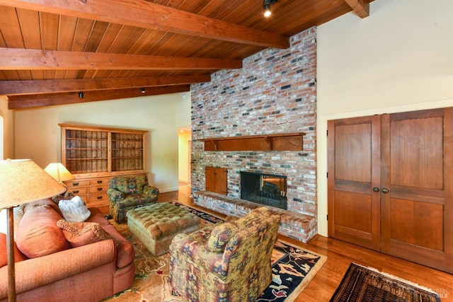 living room with vaulted ceiling with beams, wood ceiling, a brick fireplace, and wood finished floors