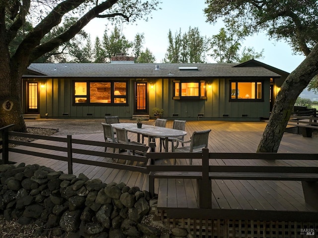 rear view of property with board and batten siding, a wooden deck, outdoor dining area, and a chimney