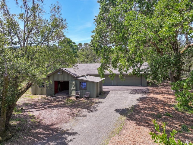 view of front facade with driveway, a shingled roof, an outdoor structure, and a garage