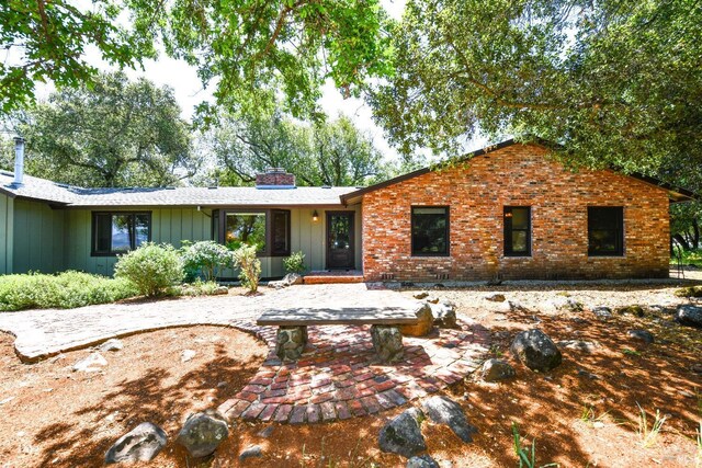 ranch-style house with board and batten siding, a chimney, and brick siding