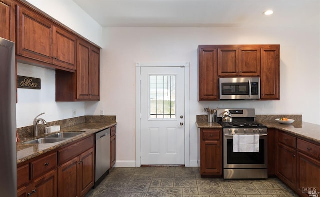 kitchen with appliances with stainless steel finishes, a sink, baseboards, dark stone countertops, and recessed lighting